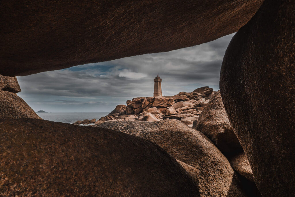 Phare de Mean Ruz lighthouse framed by granite rocks on the Pink Granite Coast in Brittany